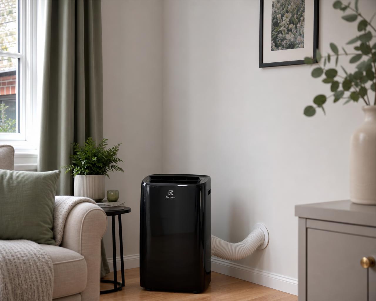 A black portable air conditioner in a British living room, its hose venting neatly through a round white wall vent with the windows closed